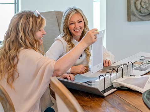 Two women sitting at a desk looking at fabric samples